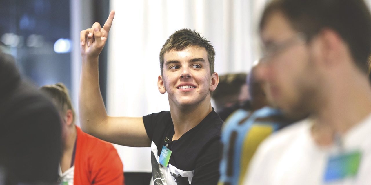 Young man, seated, raising hand